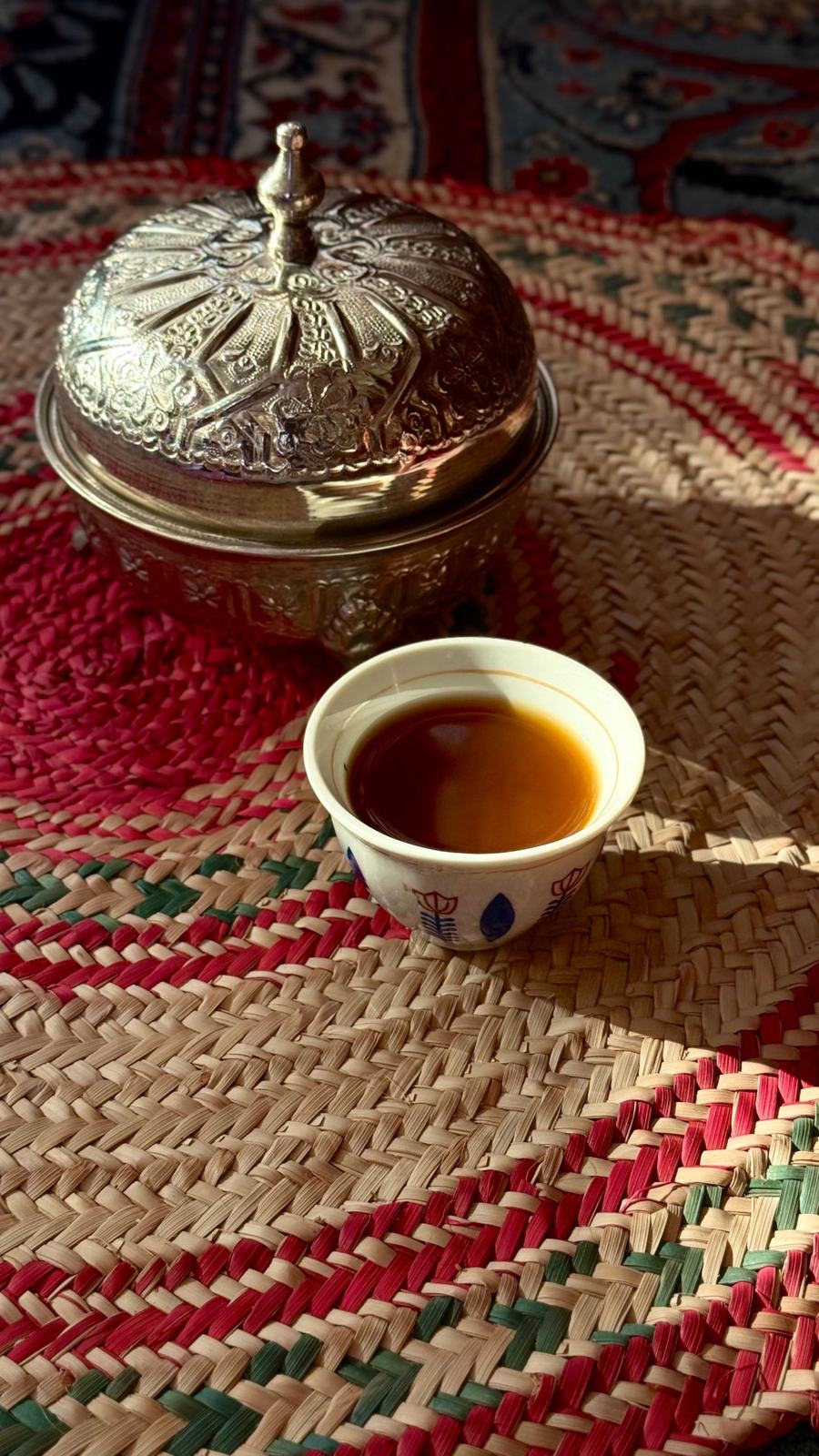 A small cup of coffee beside a brass dish on a woven mat