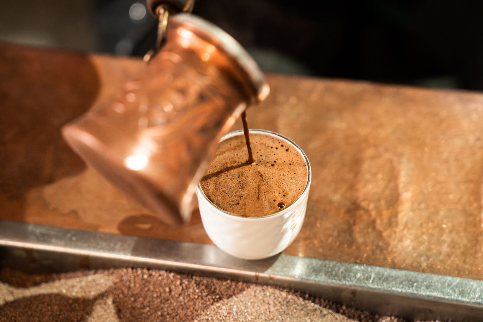 Coffee poured from a copper pot into a small white cup